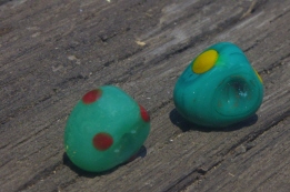 zwei dreieckige grünliche Glasperlen, Tupfen ein gelb und rot an verschiedenen Stellen des Perlenkörpers