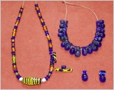 eine Glasperlenkette mit Bommelperlen, eine Glasperlenkette mit einer langen gelb-schwarzen, zahlreicdhen Bernstein- und  blauen Perlen
